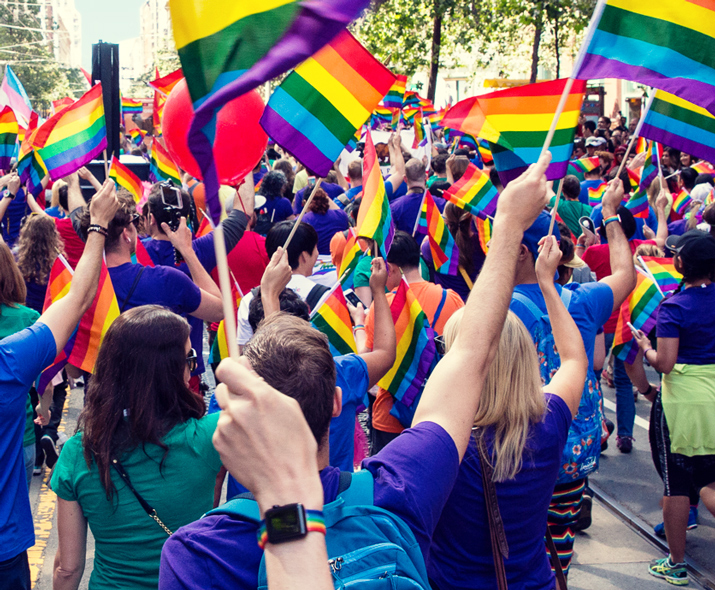 Foto af en parade med mange mennesker, som vifter med regnbueflag. 