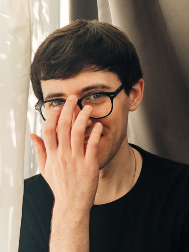 Fotoportrett av Matthew, som smiler mot leseren mens han justerer brillene.