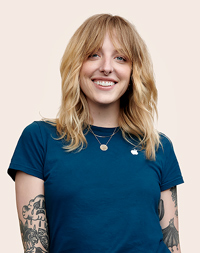 Empleada de Apple Retail con tatuajes en los brazos, sonríe a la cámara.