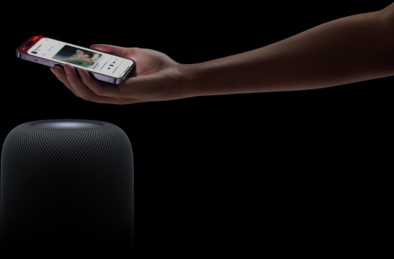 Een hand die van rechts het beeld in komt en een iPhone boven een HomePod-speaker houdt