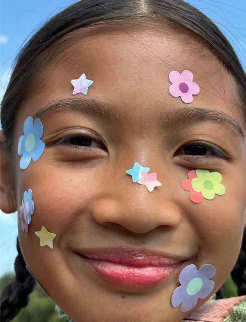 Primer plano de una niña con pegatinas de flores en la cara hecho con el zoom continuo del iPhone 15