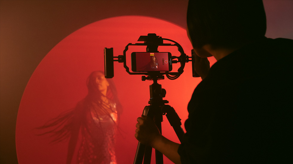 Fotografía de una persona con un iPhone colocado sobre un trípode grabando un vídeo a todo color de una mujer