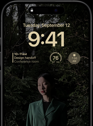 iPhone 15 Pro Always-On displejā redzams bloķēšanas ekrāns ar kalendāra vidžetu, laikapstākļu vidžetu un modinātāja vidžetu