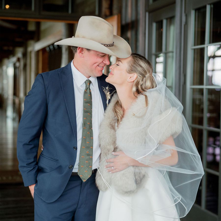 groom wearing cowboy hat and bride wearing white dress looking at eachother 