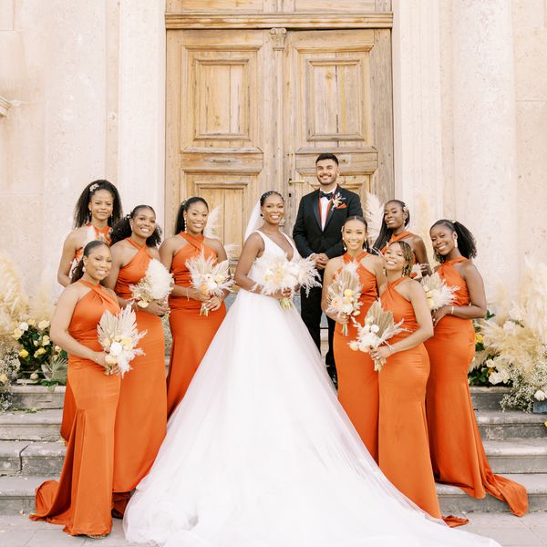 Bridesmaids in orange dresses carrying boho bouquets with dried palm leaves