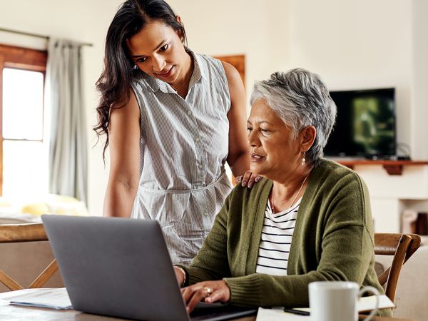young woman helping her grandmother with her finances on a laptop in their home