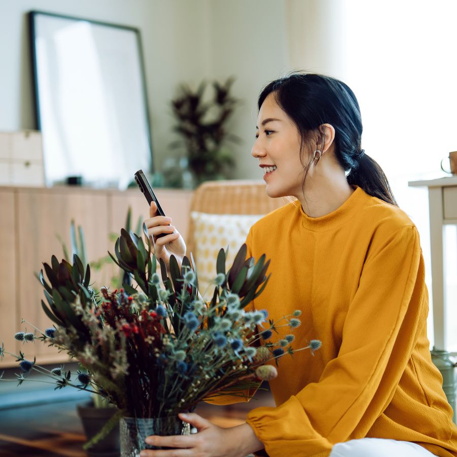 young woman receiving bouquet of fresh flower delivery from boyfriend, chatting on video call with smartphone