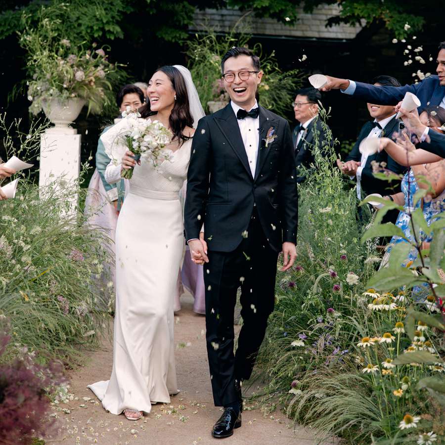 Bride and Groom Smiling During Outdoor Wedding Ceremony Recessional While Guests Toss Flower Petals