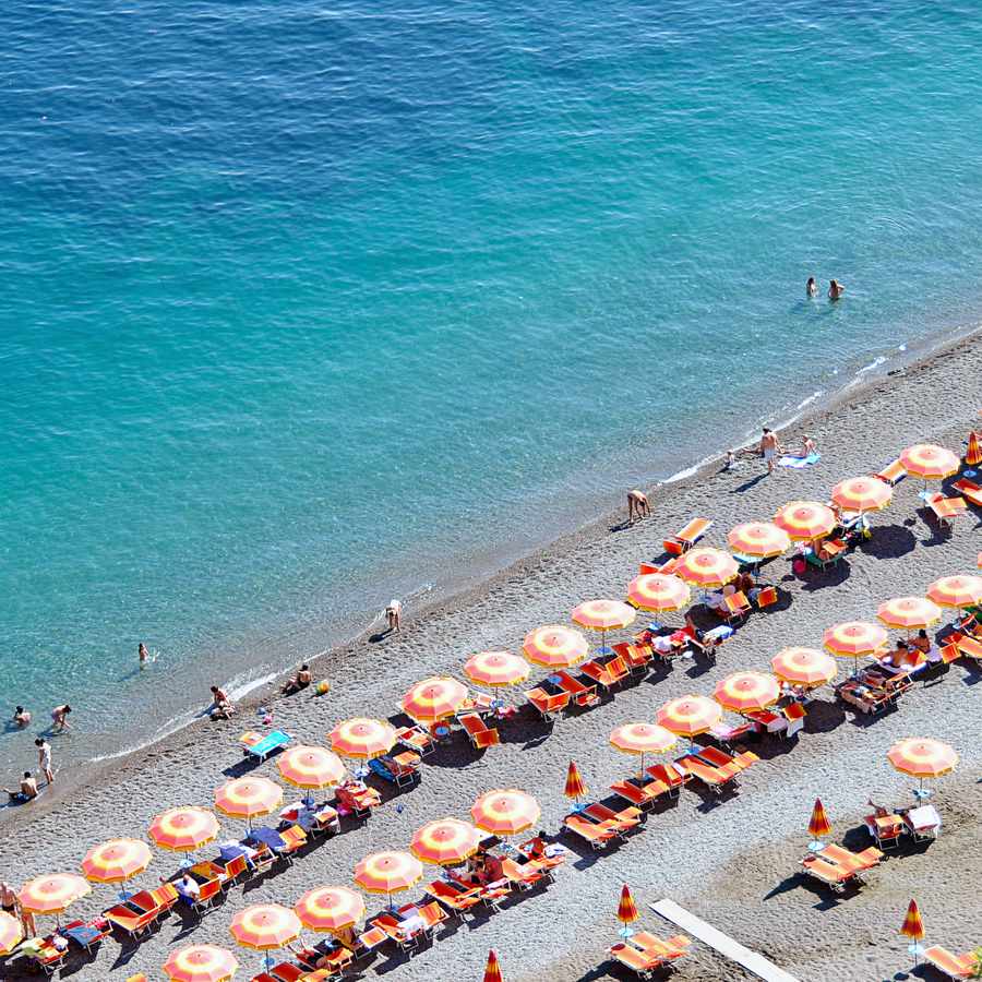 A beach in Positano, Italy, with rows of orange umbrellas in front of the Mediterranean Sea on a sunny day.