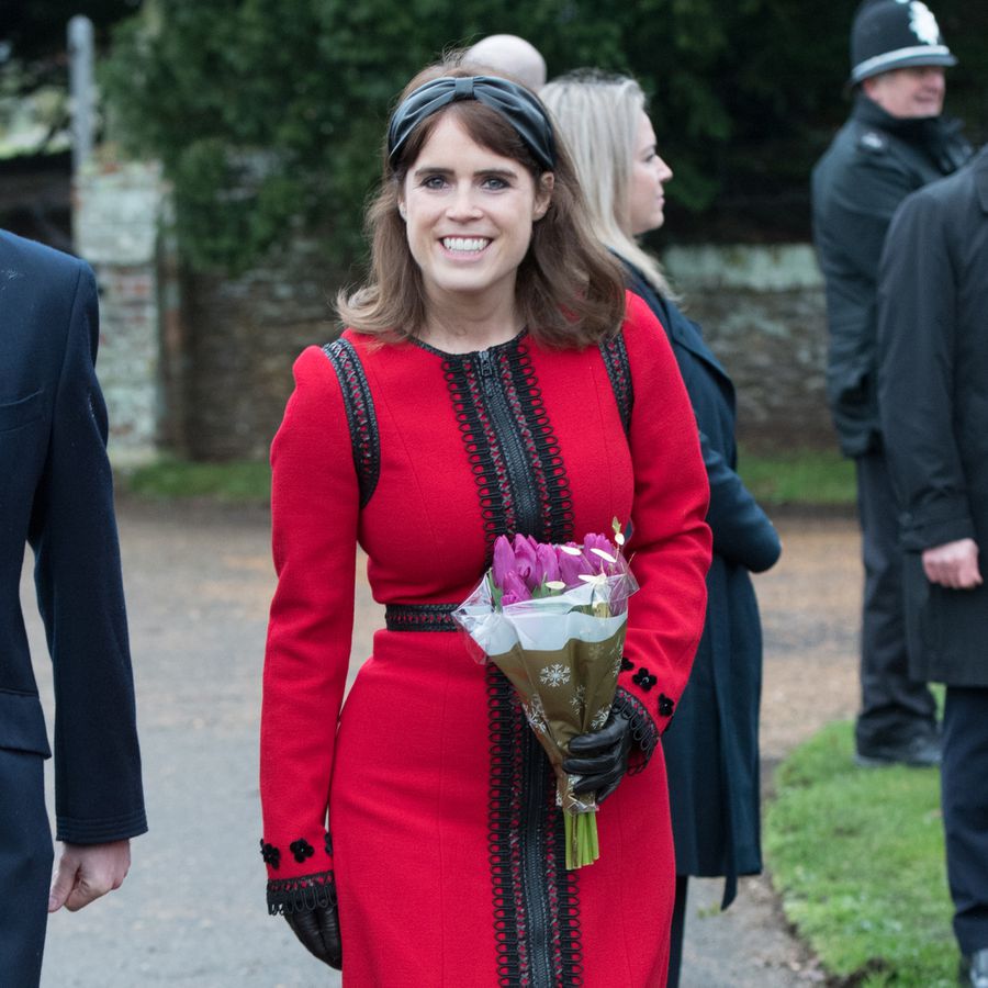 Princess Eugenie in a red dress and holding a bouquet of flowers on Christmas Day