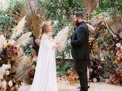 Bride and groom standing at the altar in front of dried palm leaves, pampas grass, and fall flowers during the ceremony