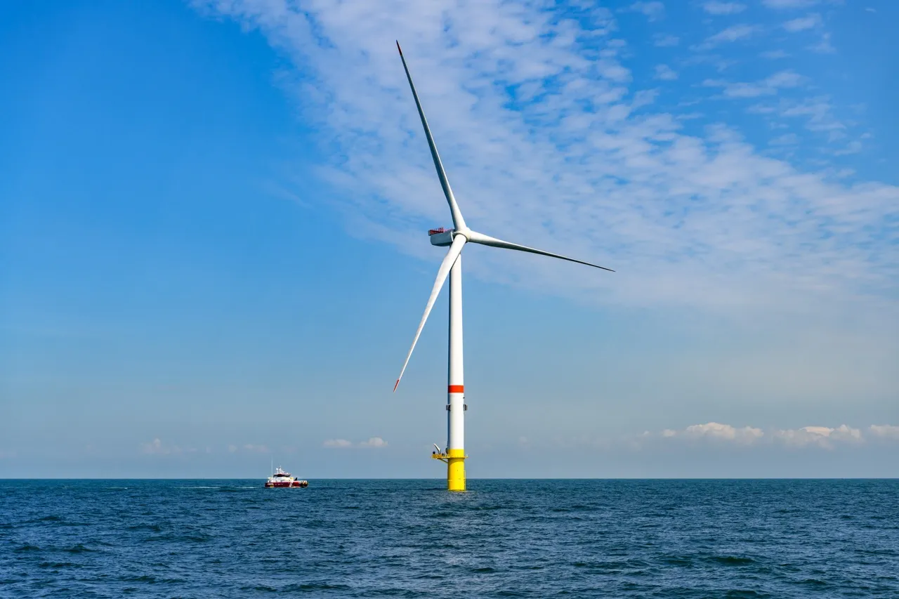 An offshore windmill in the ocean with a bright blue sky in the background