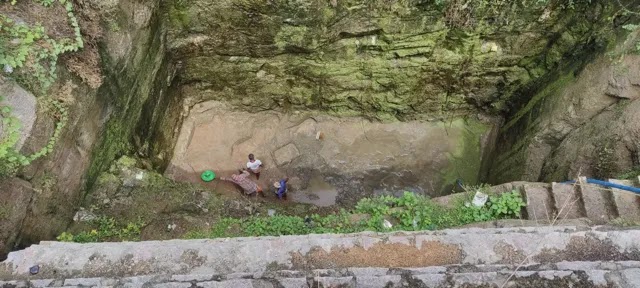 Three people clean the bottom of a water well.
