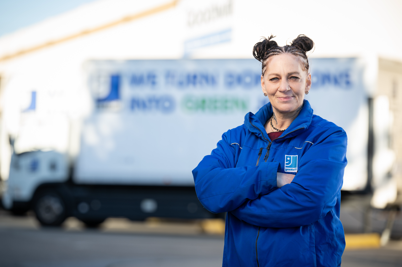 Woman in blue Goodwill branded jacket smiling in front of a truck
