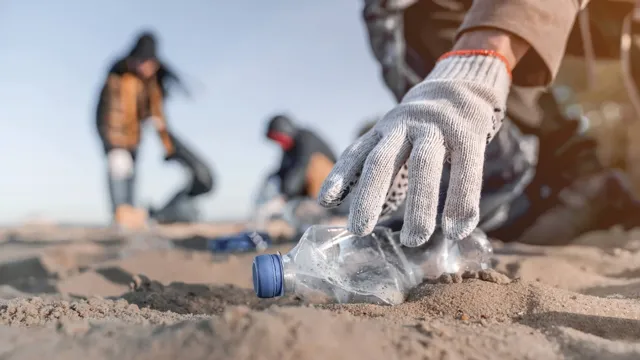 A person wearing a grey gardening glove picking up a plastic waterbottle on the beach