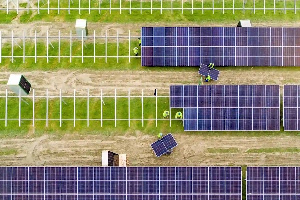 Group of workers asemble rows of solar panels in a green field