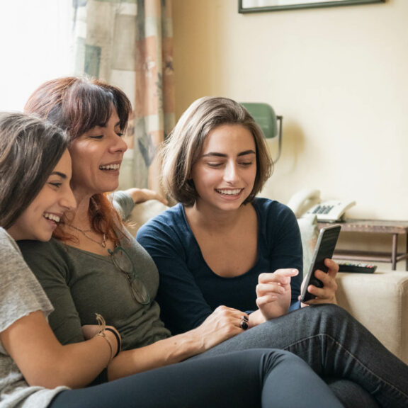 Mère et filles sur le canapé souriantes devant un smartphone