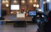 Femme d'affaires et homme d'affaires faisant une présentation lors d'un séminaire en ligne, assis sur des fauteuils sur la scène, tenant des microphones. Caméra vidéo au premier plan.