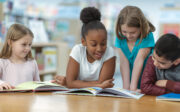 Un groupe d'amis est assis à une table dans leur classe. Ils lisent un livre ensemble en souriant et en riant.