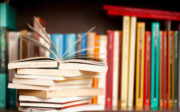 Pile de livres sur une étagère de bibliothèque en bois, l'un d'eux ouvert sur le dessus, fond de dos de livre multicolore.