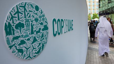 Des participants passent devant un logo de la COP28 à Dubaï, le 3 décembre 2023. (GIUSEPPE CACACE / AFP)