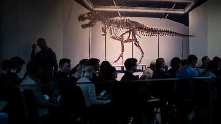Des enchérisseurs, assis à côté d'une photo de "Trinity" lors de la vente du squelette du Tyrannosaurus-Rex (T-Rex) par la maison de vente aux enchères Koller à Zurich, en Suisse, le 18 avril 2023. (FABRICE COFFRINI / AFP)