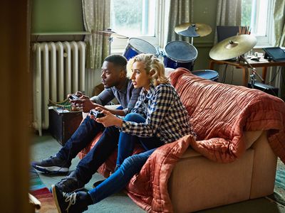 Two young adults playing console video games sitting on a couch in a small apartment.
