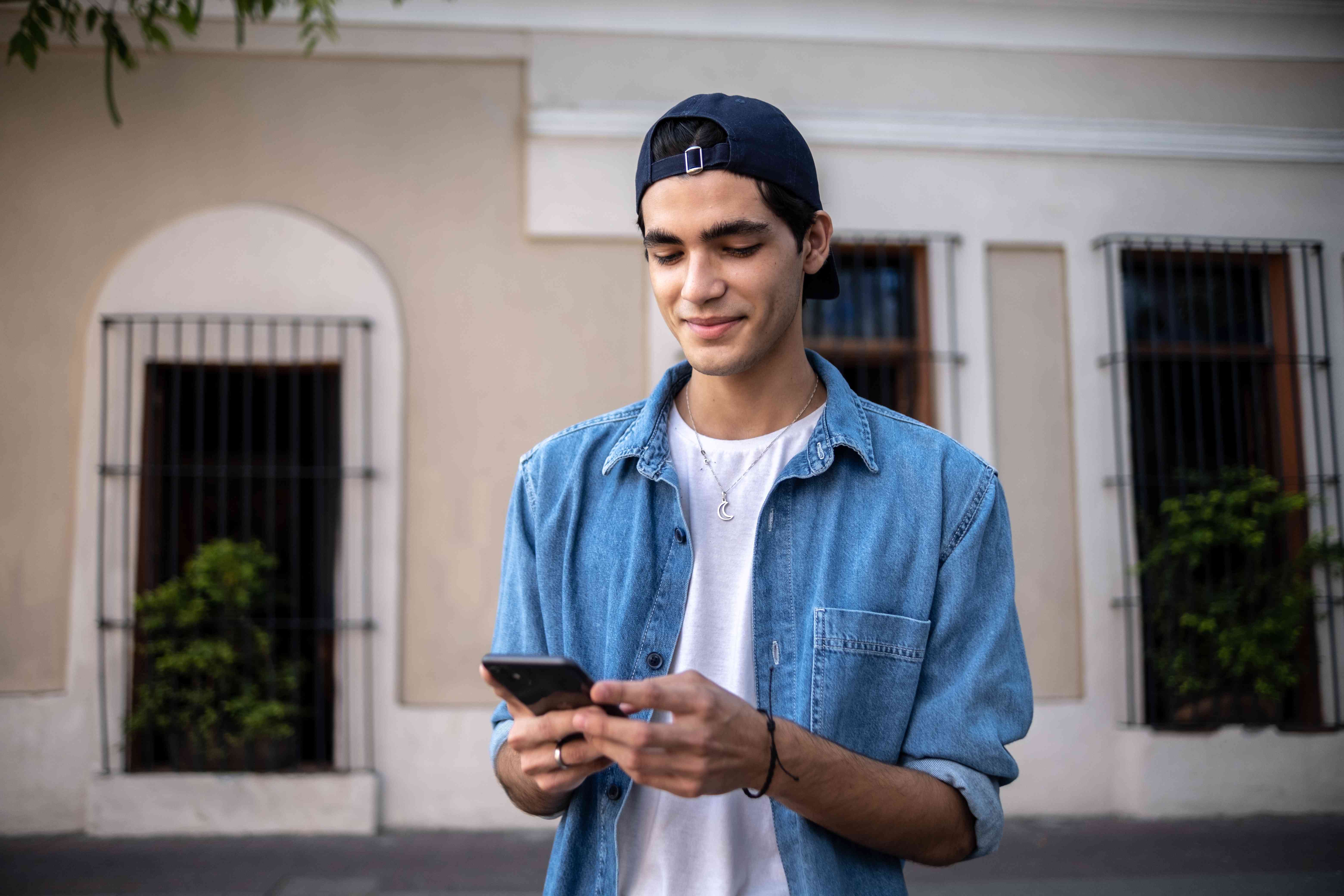 Young latino man smiling as he looks at his smartphone