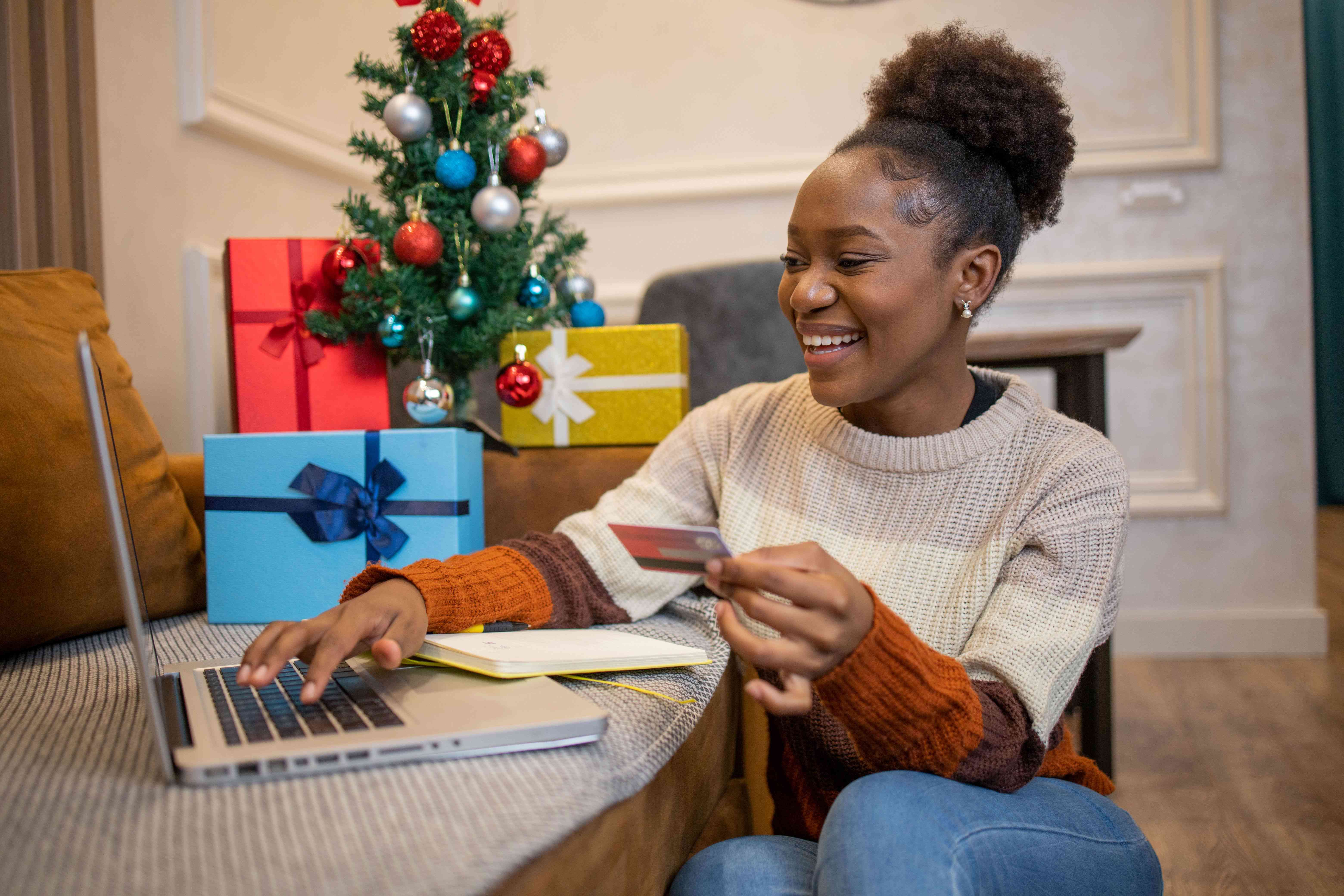 Woman shopping online with a laptop near a Christmas tree with presents