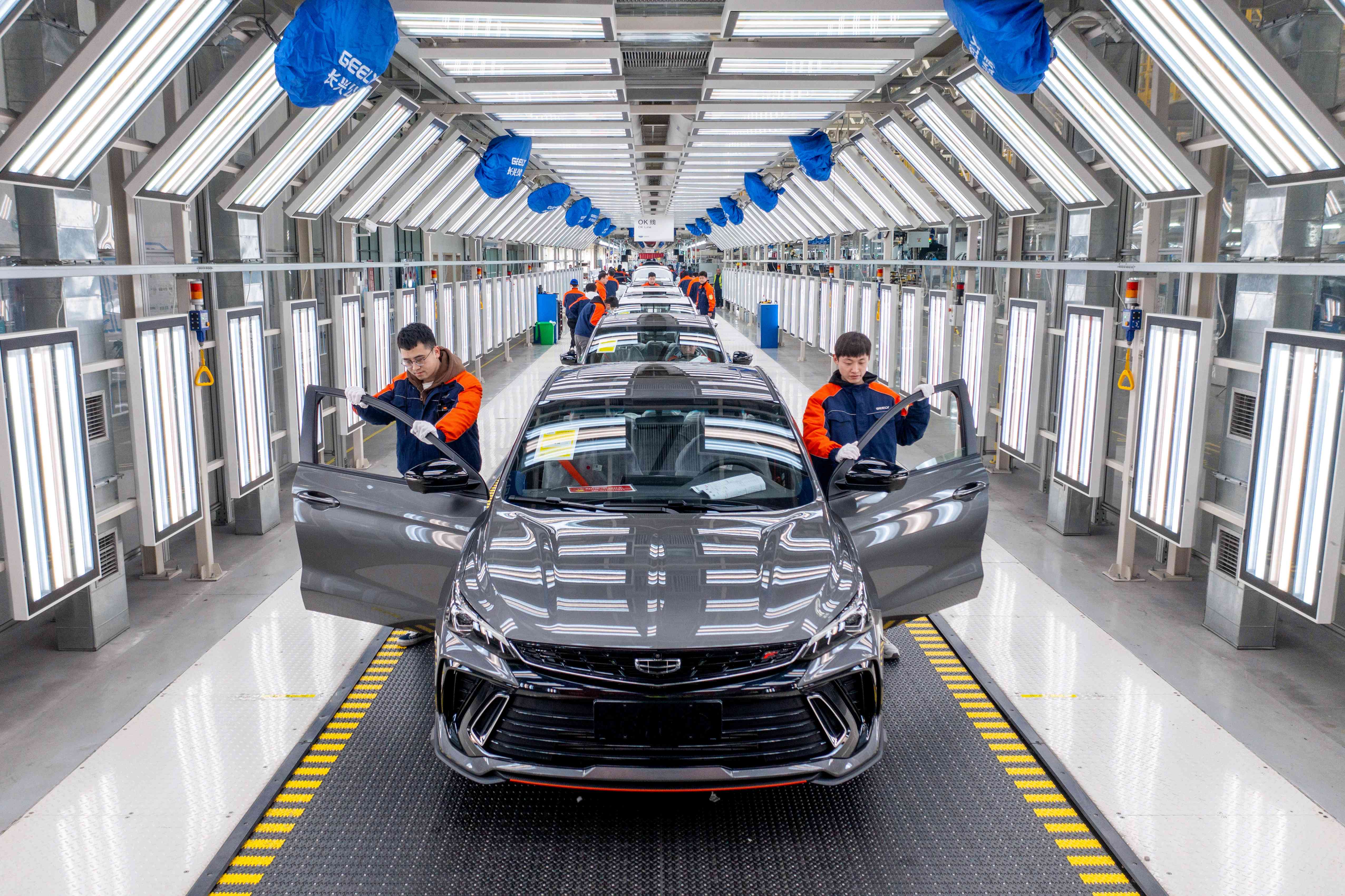 Two people on either side of a new car in a manufacturing facility in China.