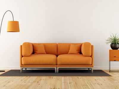 Orange sofa with cushions, rug, orange lamp, and orange side table against white wall.