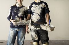 mid-section of a couple doing plaster and holding plaster buckets and brushes with plaster all over their clothes
