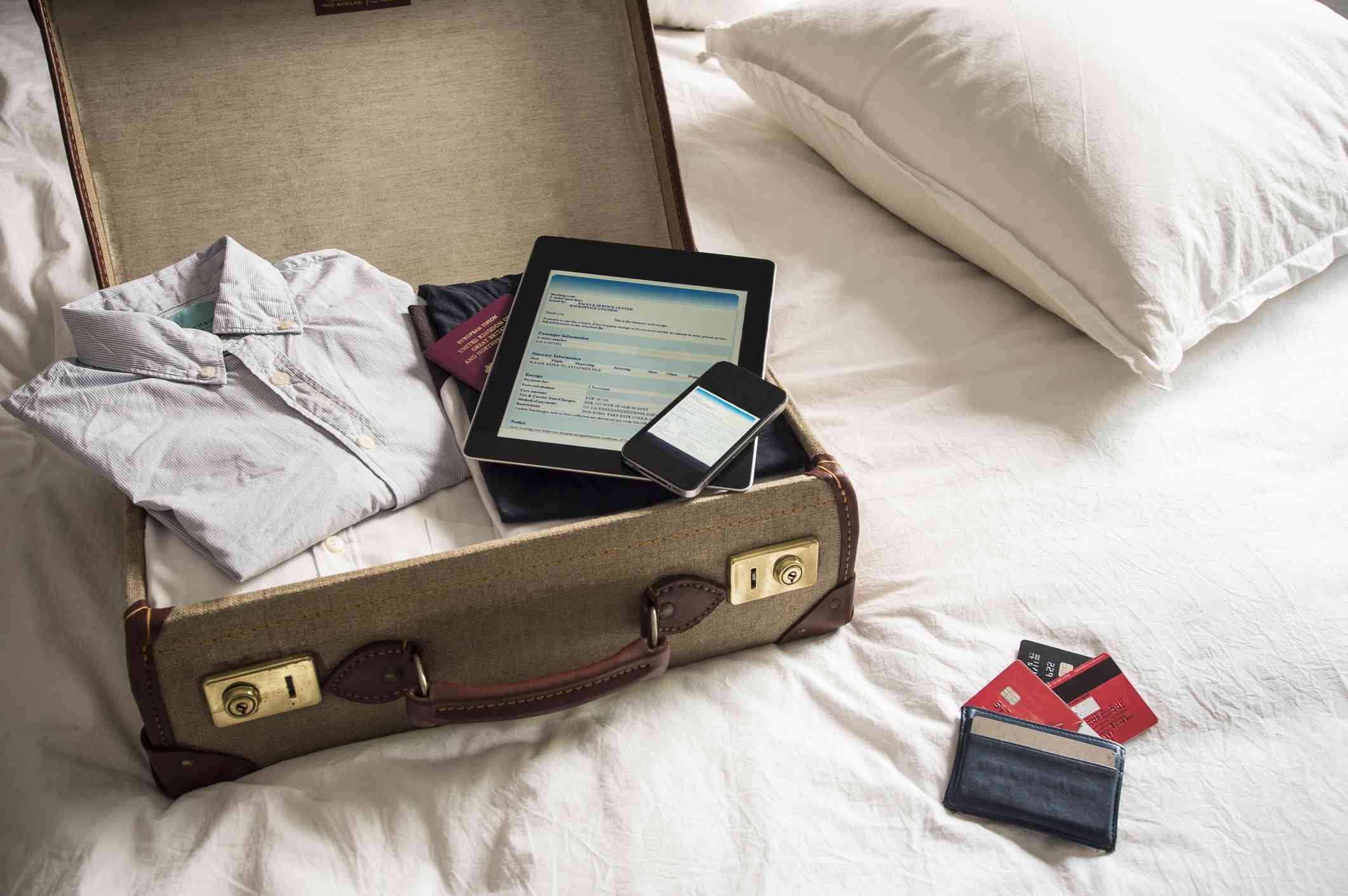 Open suitcase on bed with digital tablet and phone
