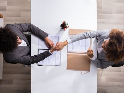 Aerial view of two business people shaking hands at a desk with papers on it