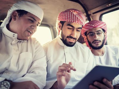 Three young Arab men in a car looking at a tablet