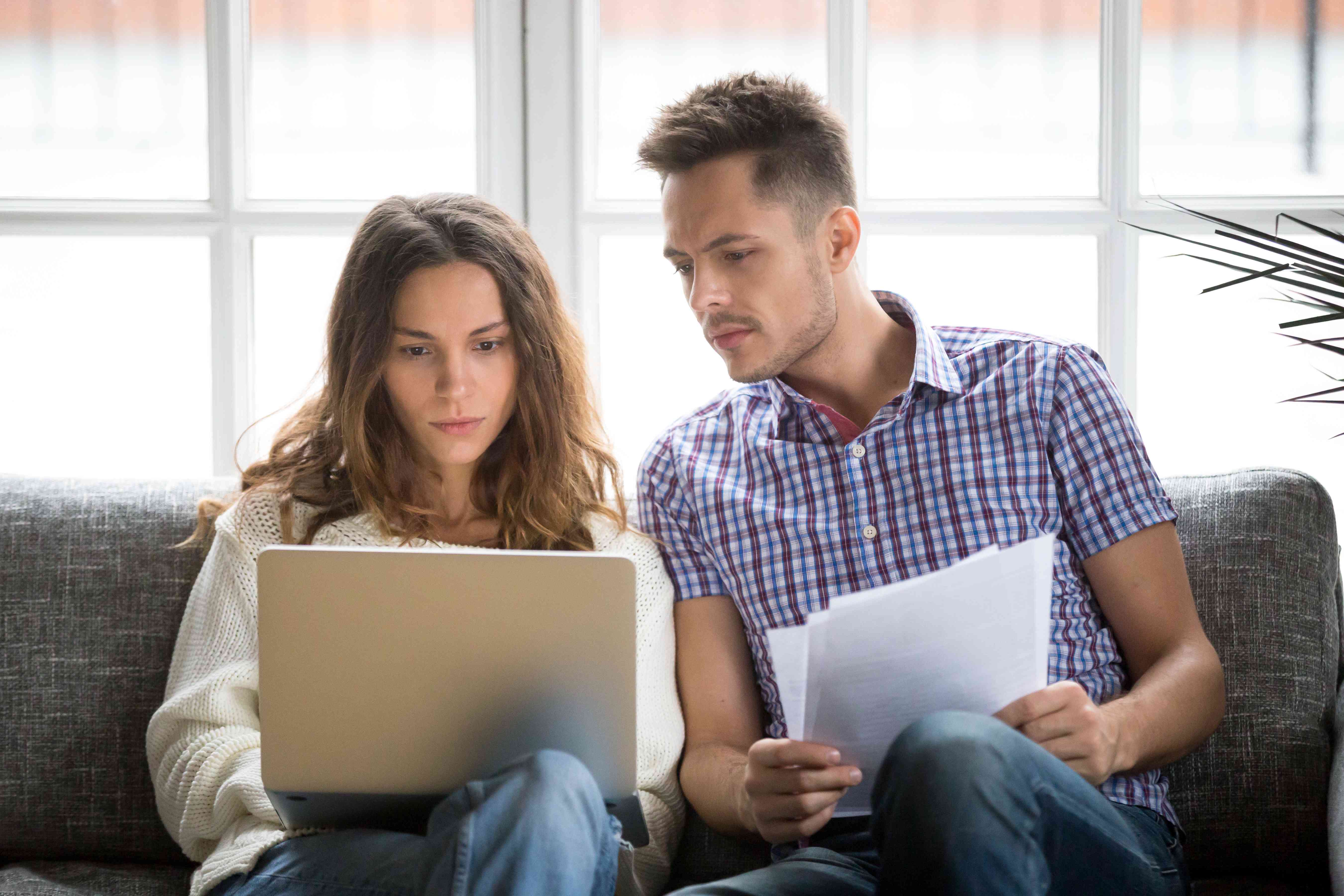 Young white couple on living room couch intently studying laptop together