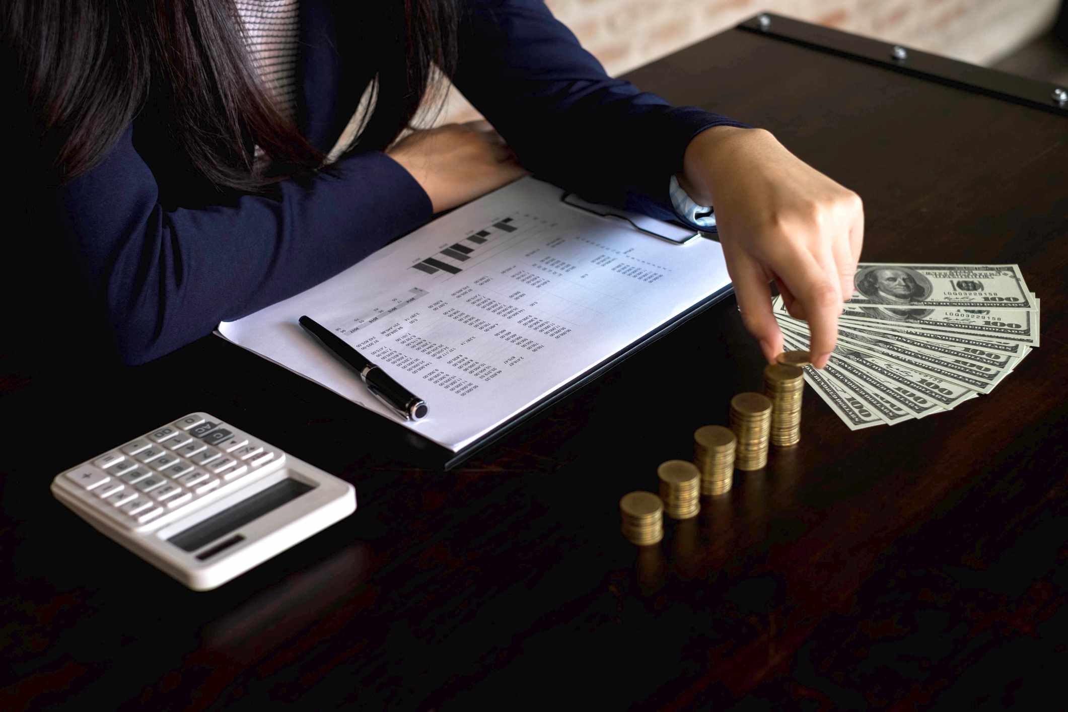 A midsection of businesswoman stacking coins on desk in office.