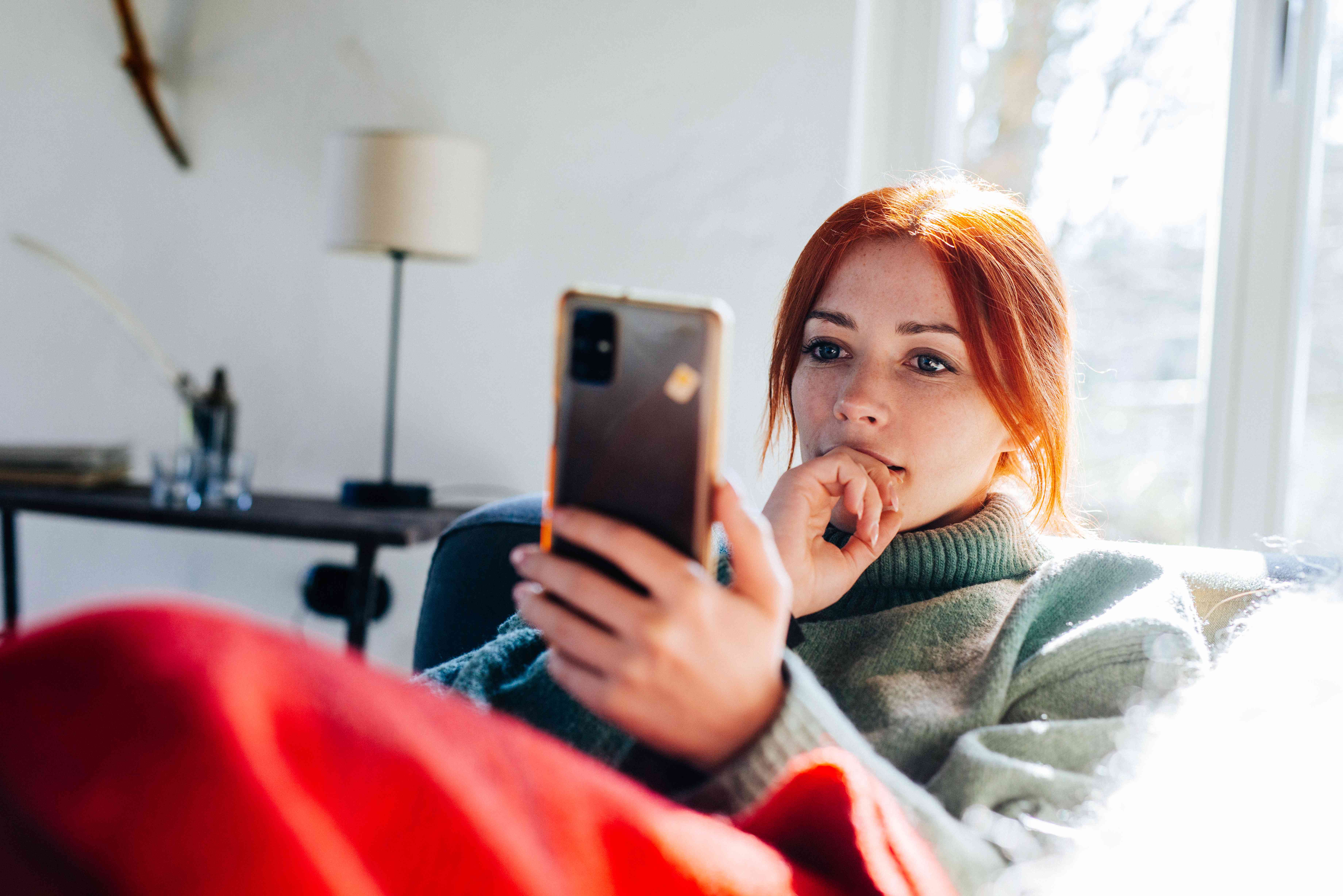 Young woman at home intently pondering something on her smartphone