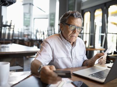 Focused senior restaurant owner paying bills at laptop