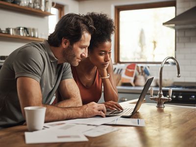 Young couple at their kitchen island looking together at a laptop with financial papers spread out