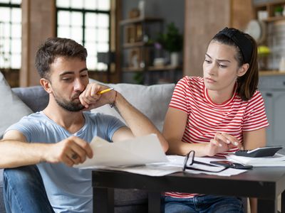 Young couple at home looking concerned as they review papers and use a calculator