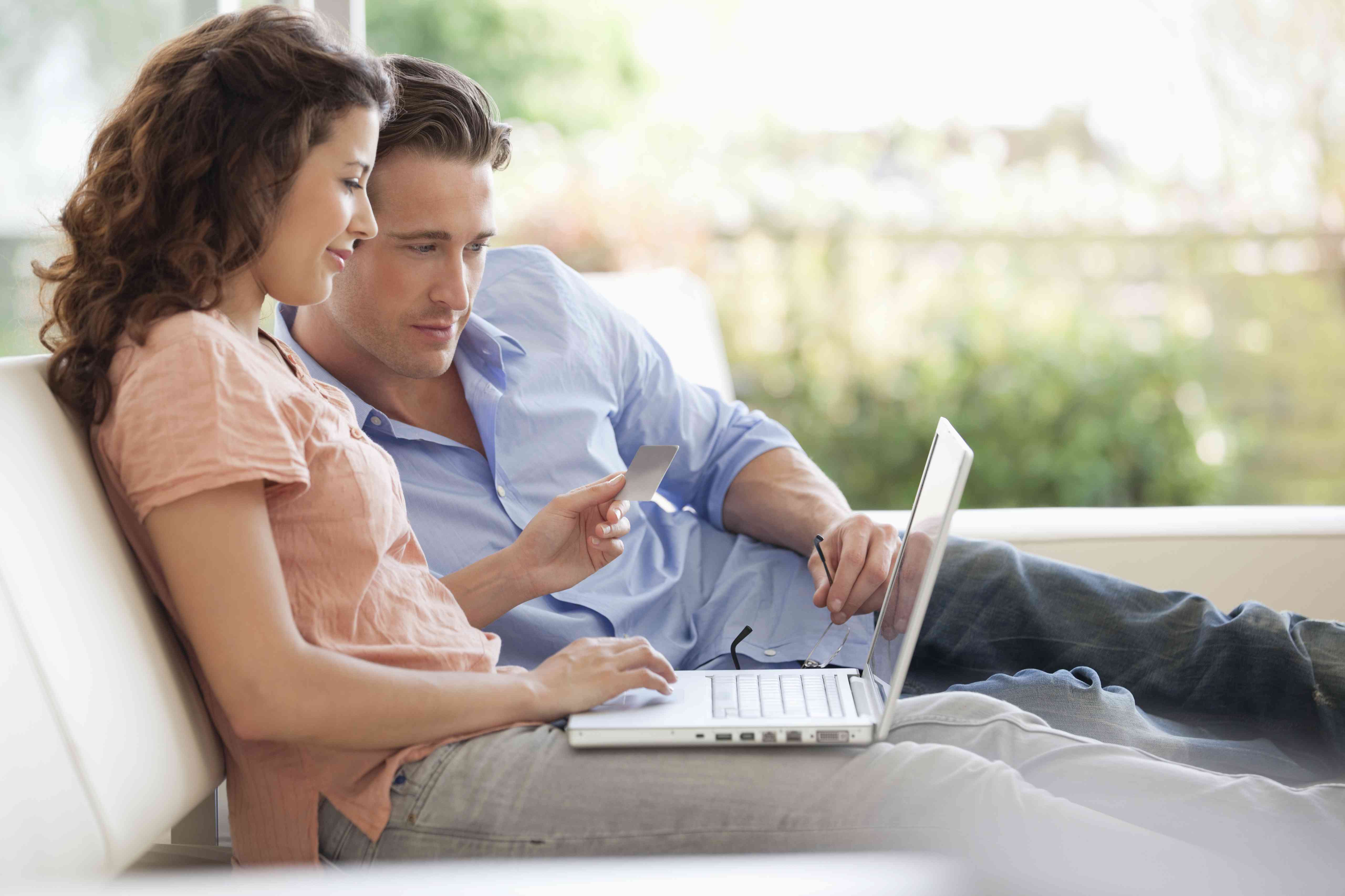 A man and a woman sit on a couch with a laptop paying for something with a credit card