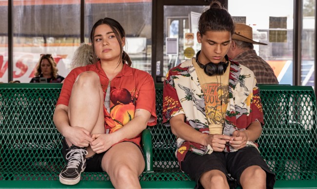 A teen boy and girl in Hawaiian shirts sit next to each other on a green indoor bench; still from "Reservation Dogs"