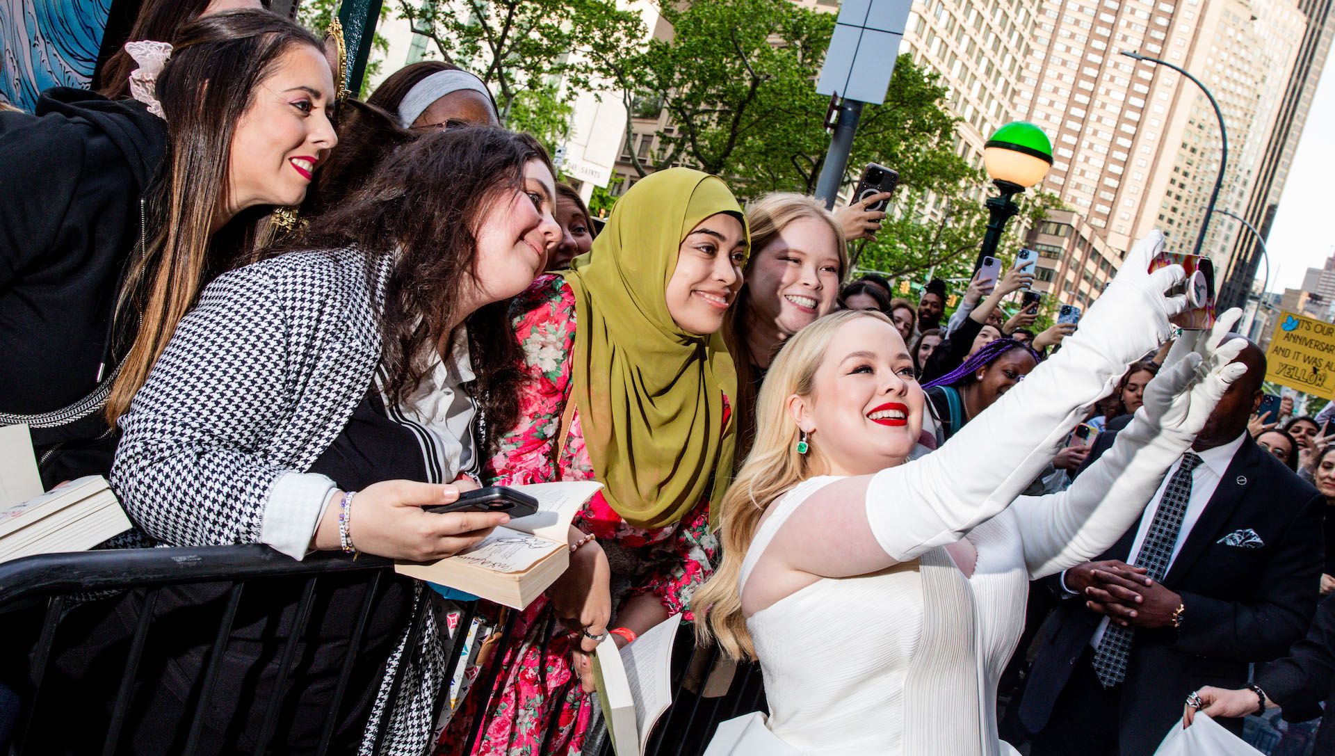 Actor Nicola Coughlan wearing a white dress and taking selfies with fans outside.
