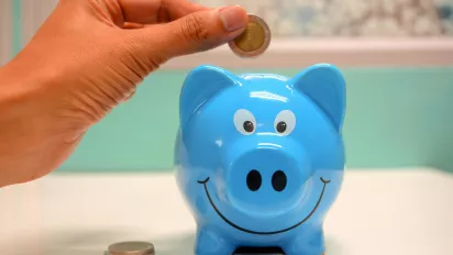 A hand putting a coin in a piggy bank.