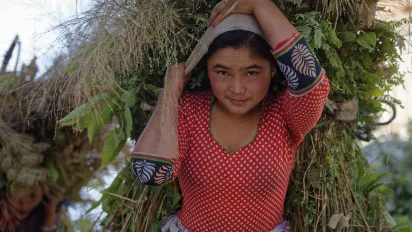 A woman carrying crops on her back and looking at the camera.