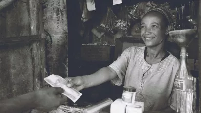 A woman at a market stand returning change and smiling.