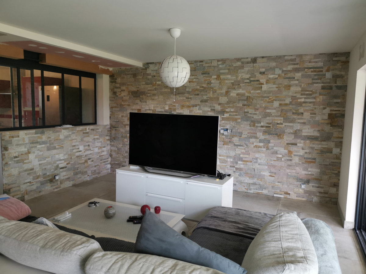 Un salon avec canapé et télé. Les murs sont en carrelage.