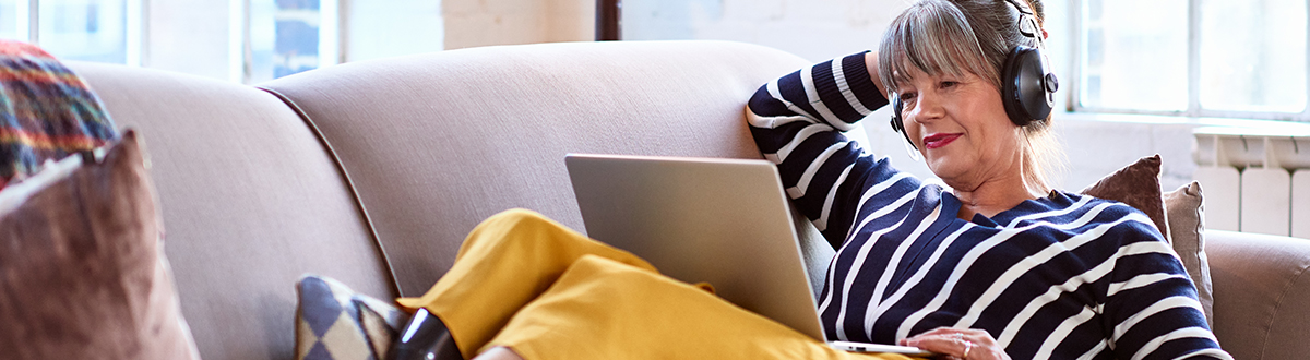 Kobieta relaksująca się na sofie i słuchająca muzyki z laptopa