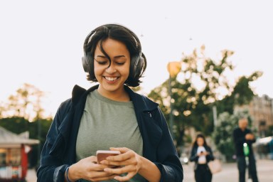 Seorang wanita mendengarkan musik dengan headphone dan berjalan di jalan